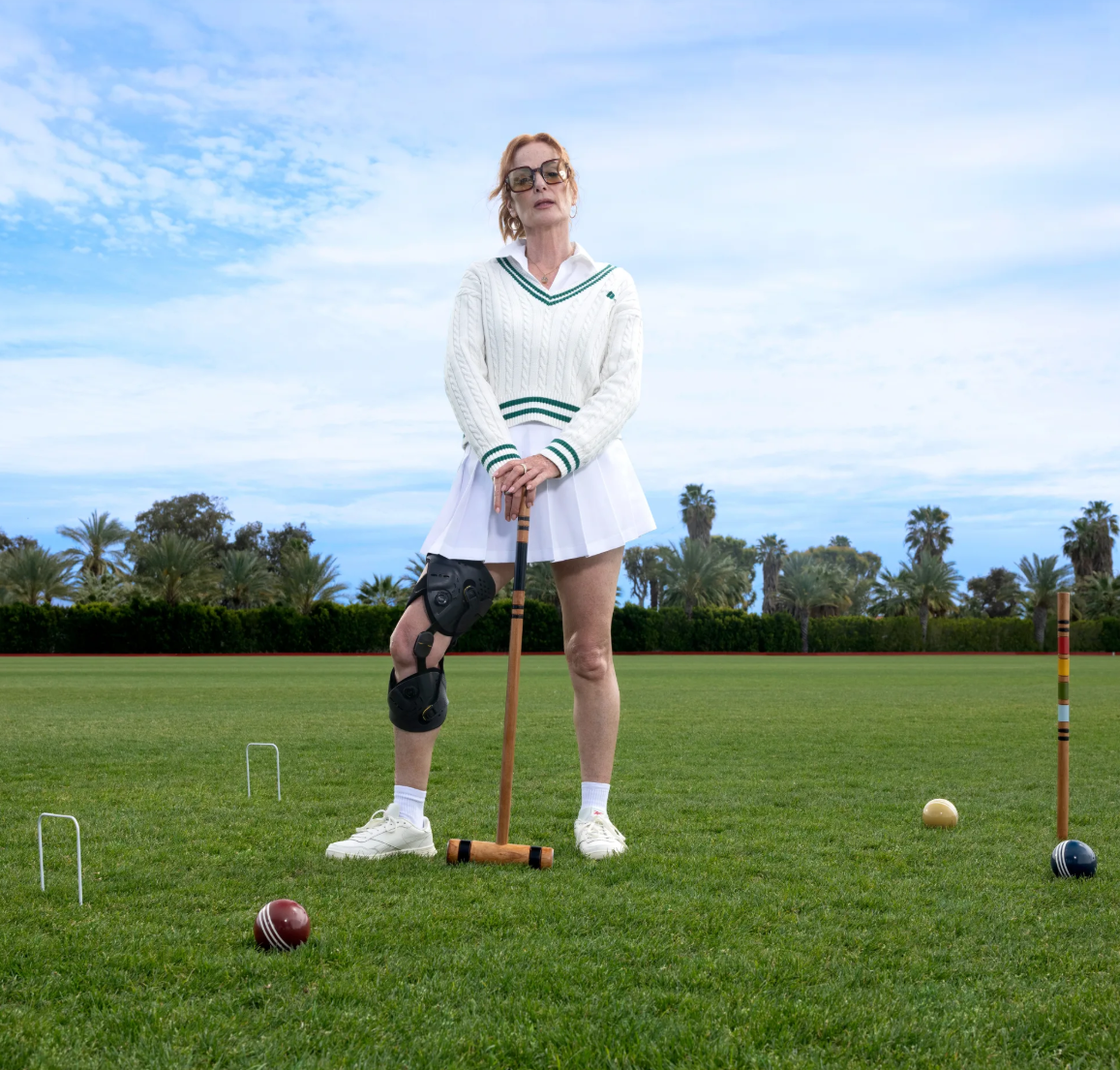 Woman playing croquet on a grassy field with a clear sky wearing Ossur Unloader One X knee brace.