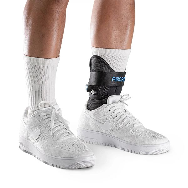 Person with white tennis shoes wearing an Aircast AirLift PTTD ankle support rear step-in design for easy donning
